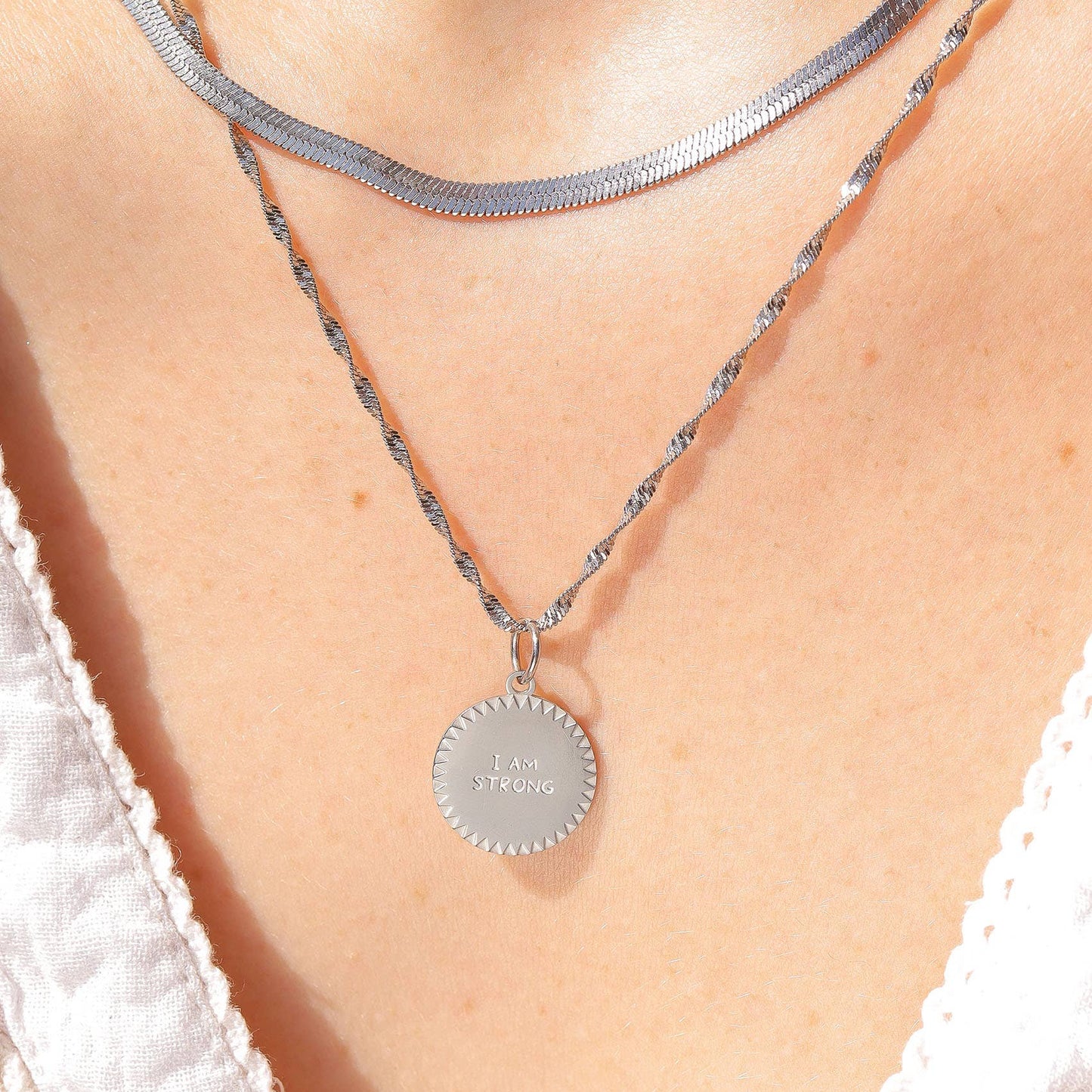 Silver necklace with a round pendant on a person wearing a white lace top.