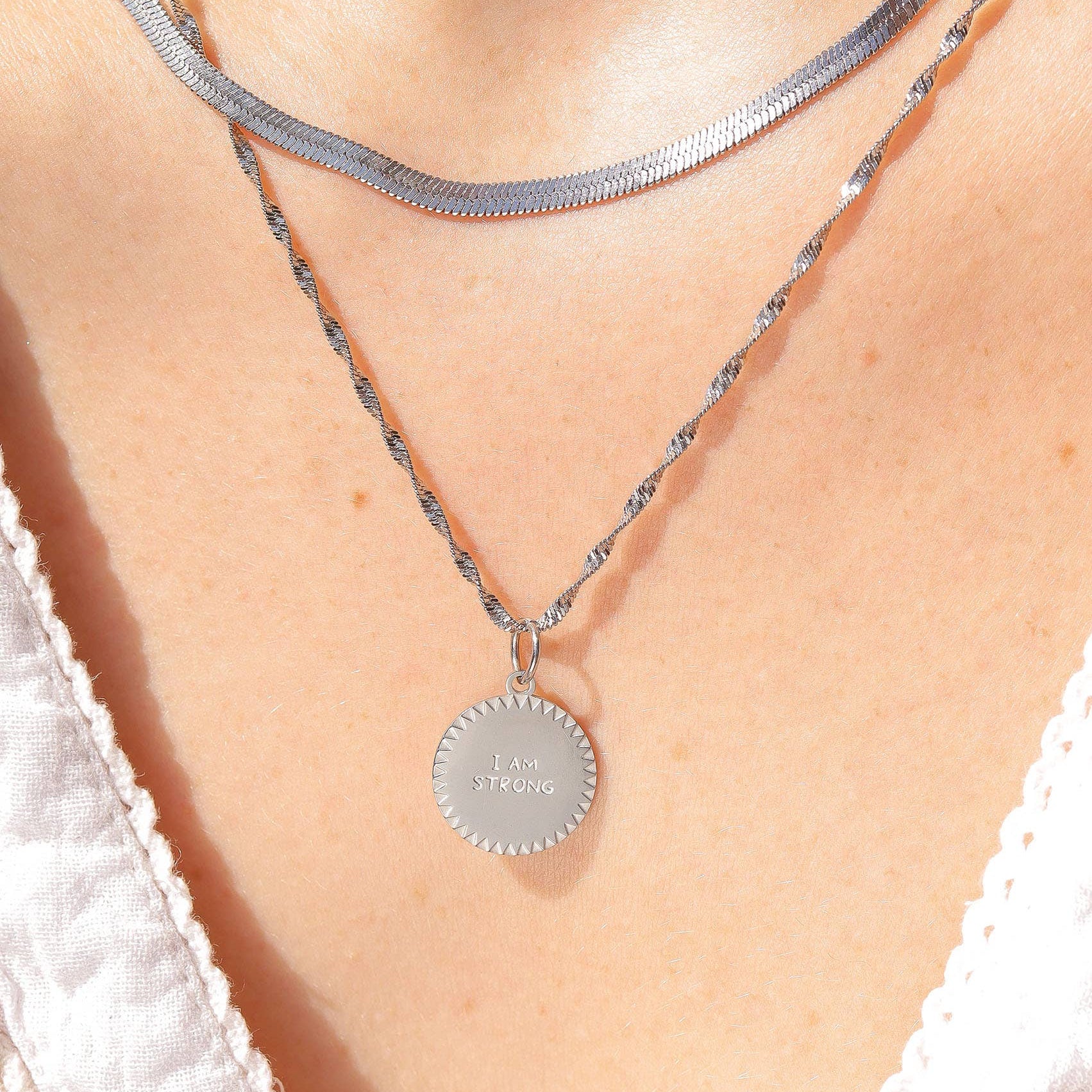 Silver necklace with a round pendant on a person wearing a white lace top.