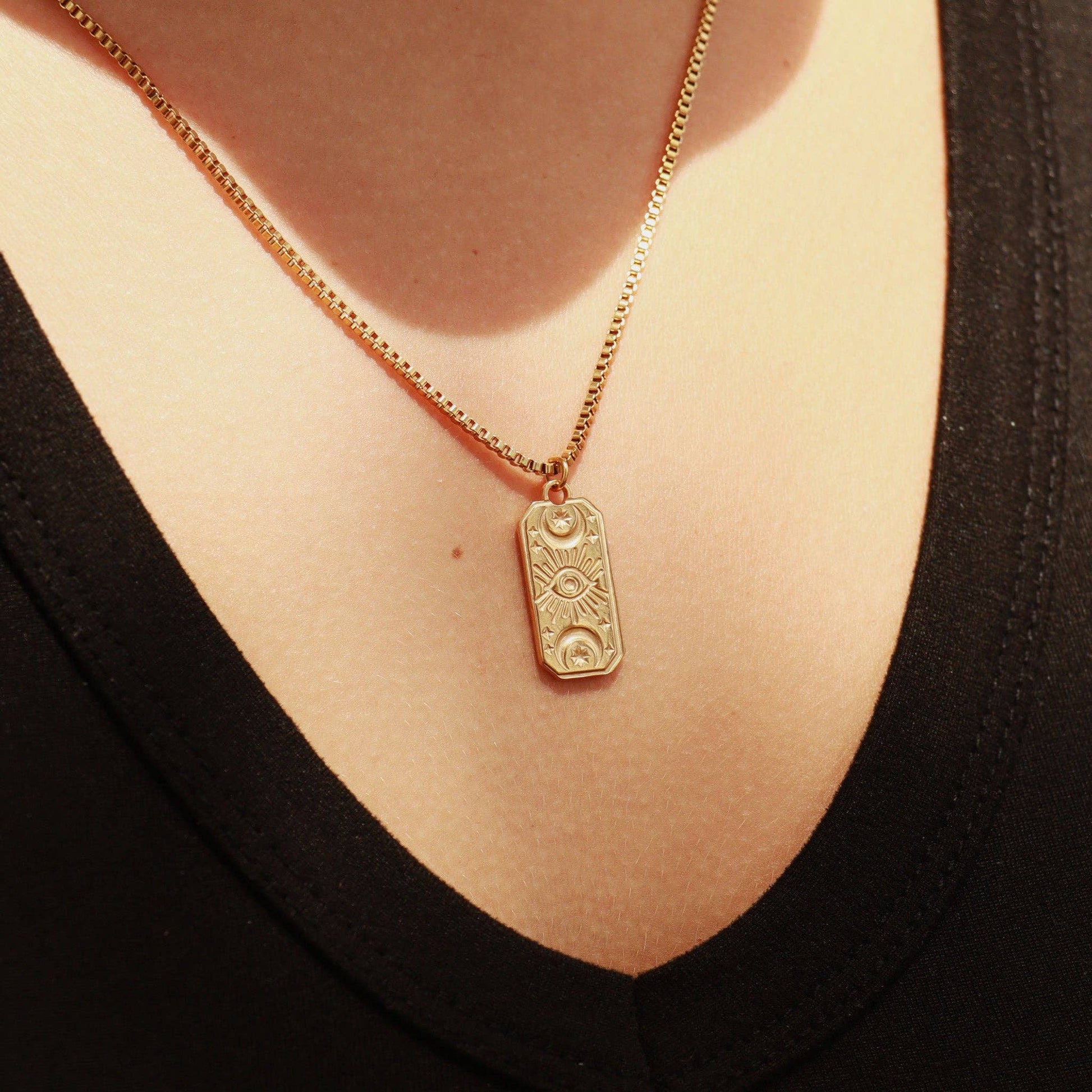 Gold necklace with a pendant on a person wearing a black top