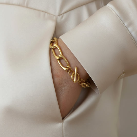 Gold chain bracelet on a wrist with a neutral background