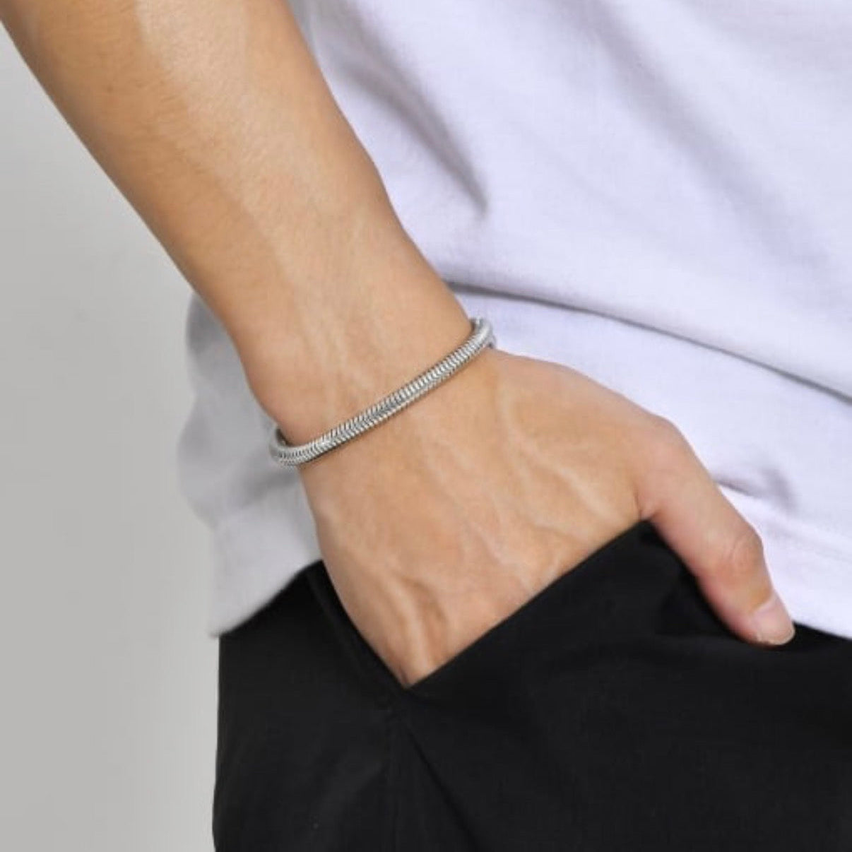 Person wearing a silver bracelet on a plain background