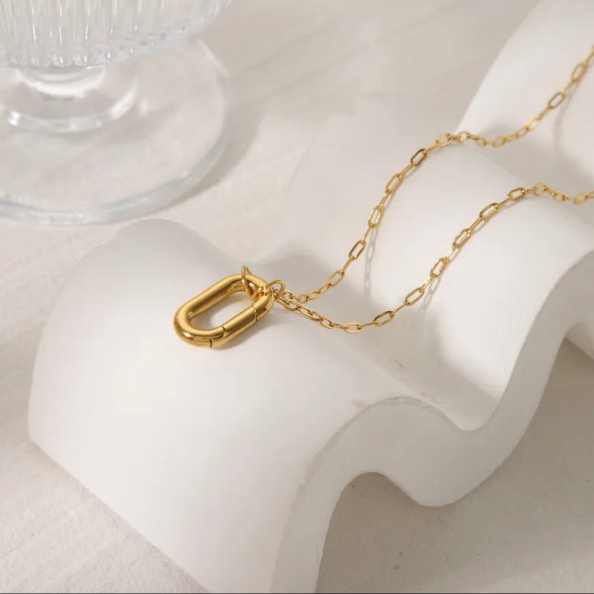 Gold chain necklace on a white stand with a clear glass object in the background