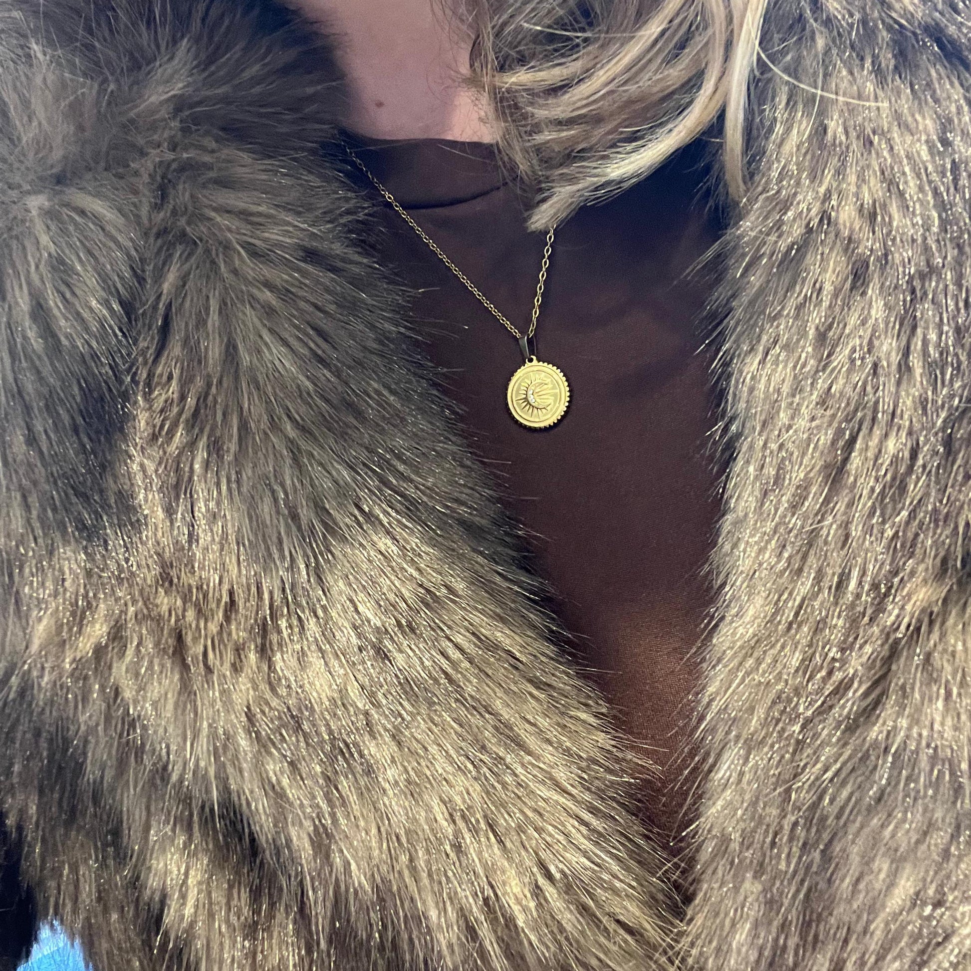 Close-up of a person wearing a fur coat with a gold necklace featuring a circular pendant.