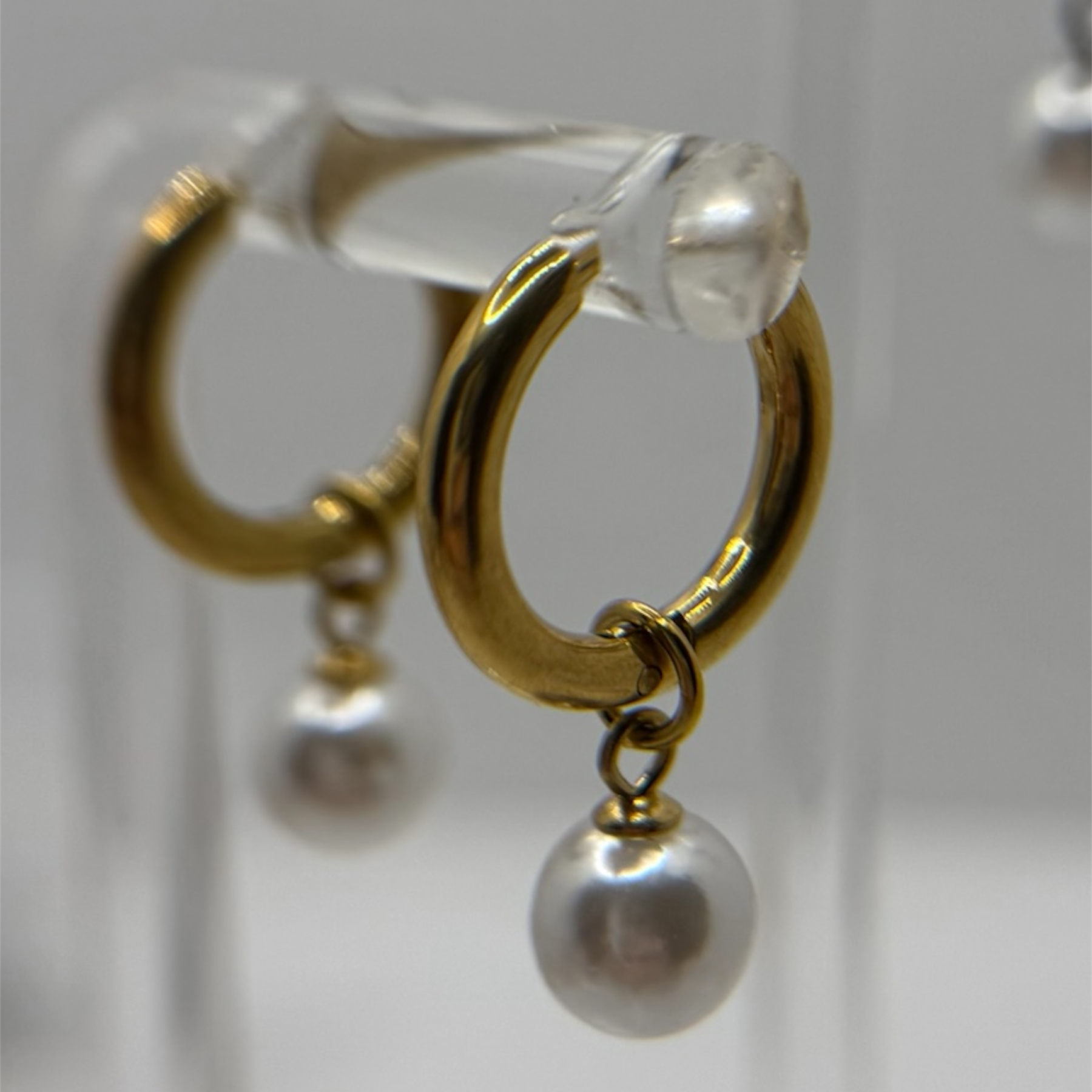 Gold hoop earrings with pearl drops on a clear stand against a light background
