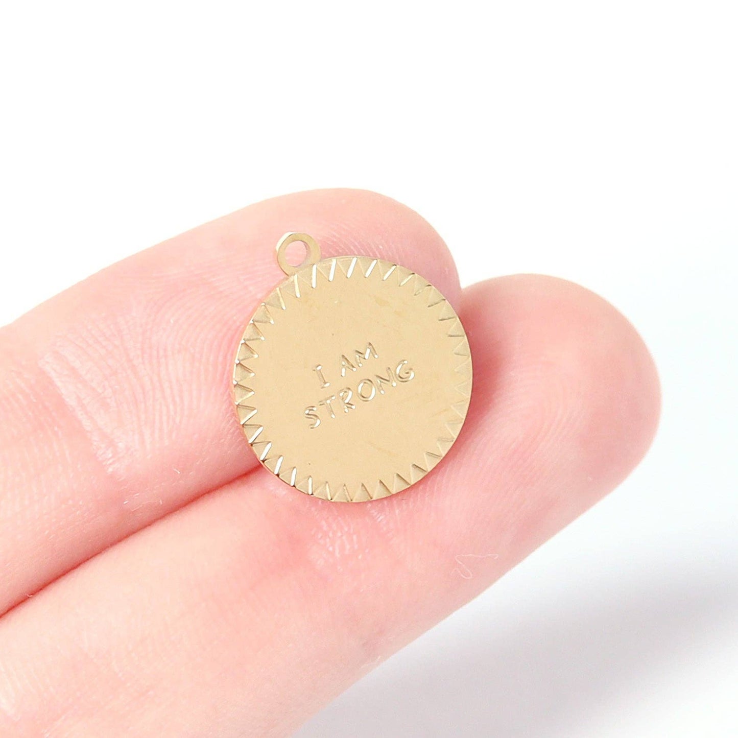 Gold pendant with 'I am a strong woman' engraving held between fingers on a white background