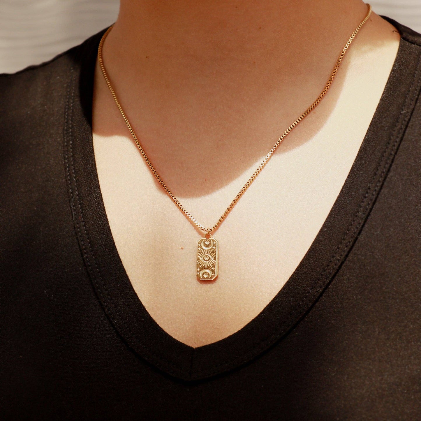 Gold necklace with a pendant worn by a person in a black top.