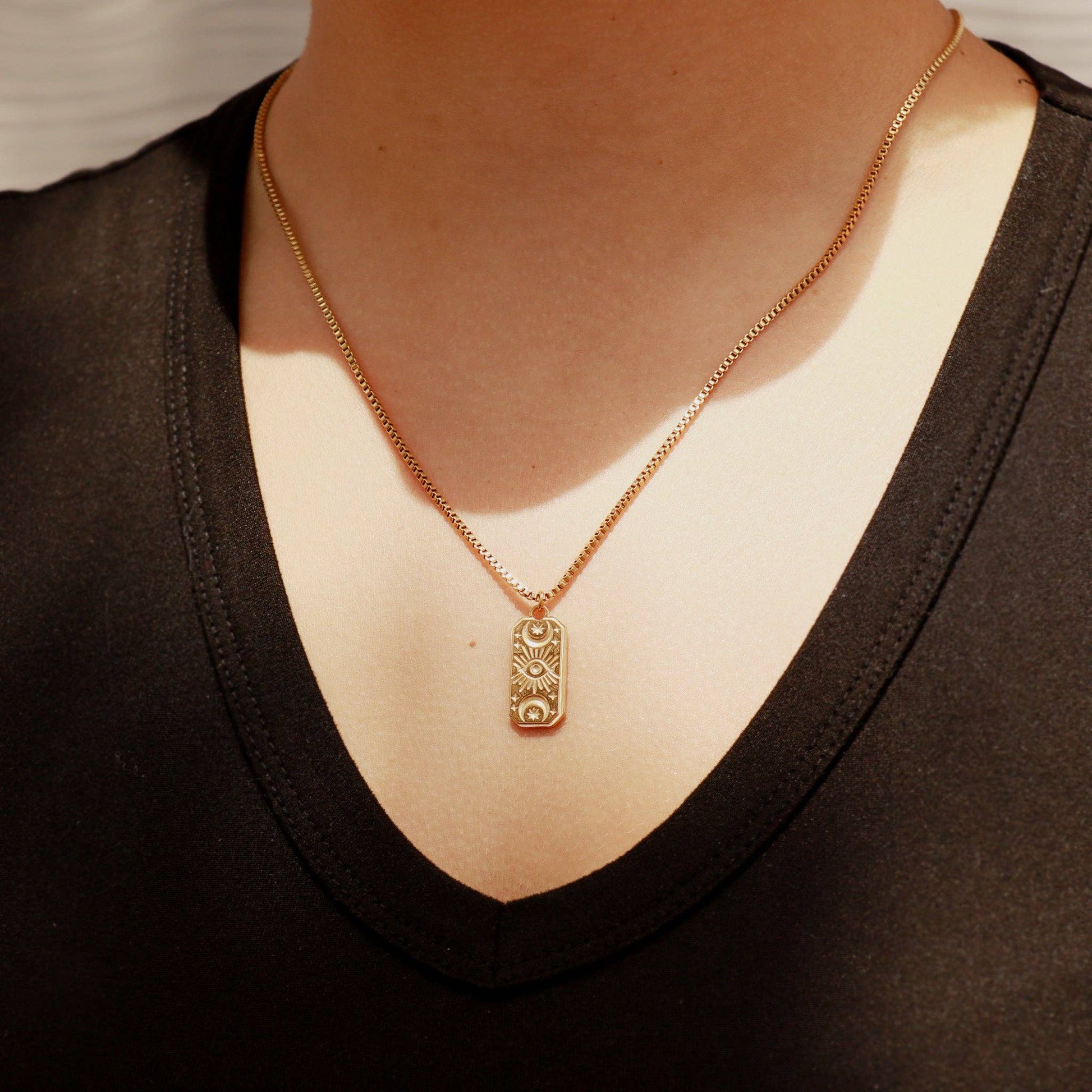 Gold necklace with a pendant worn by a person in a black top.
